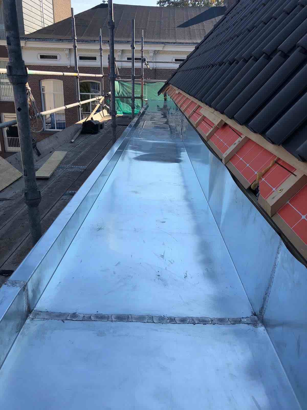 Nieuwe lange zinken dakgoot naast een pannendak