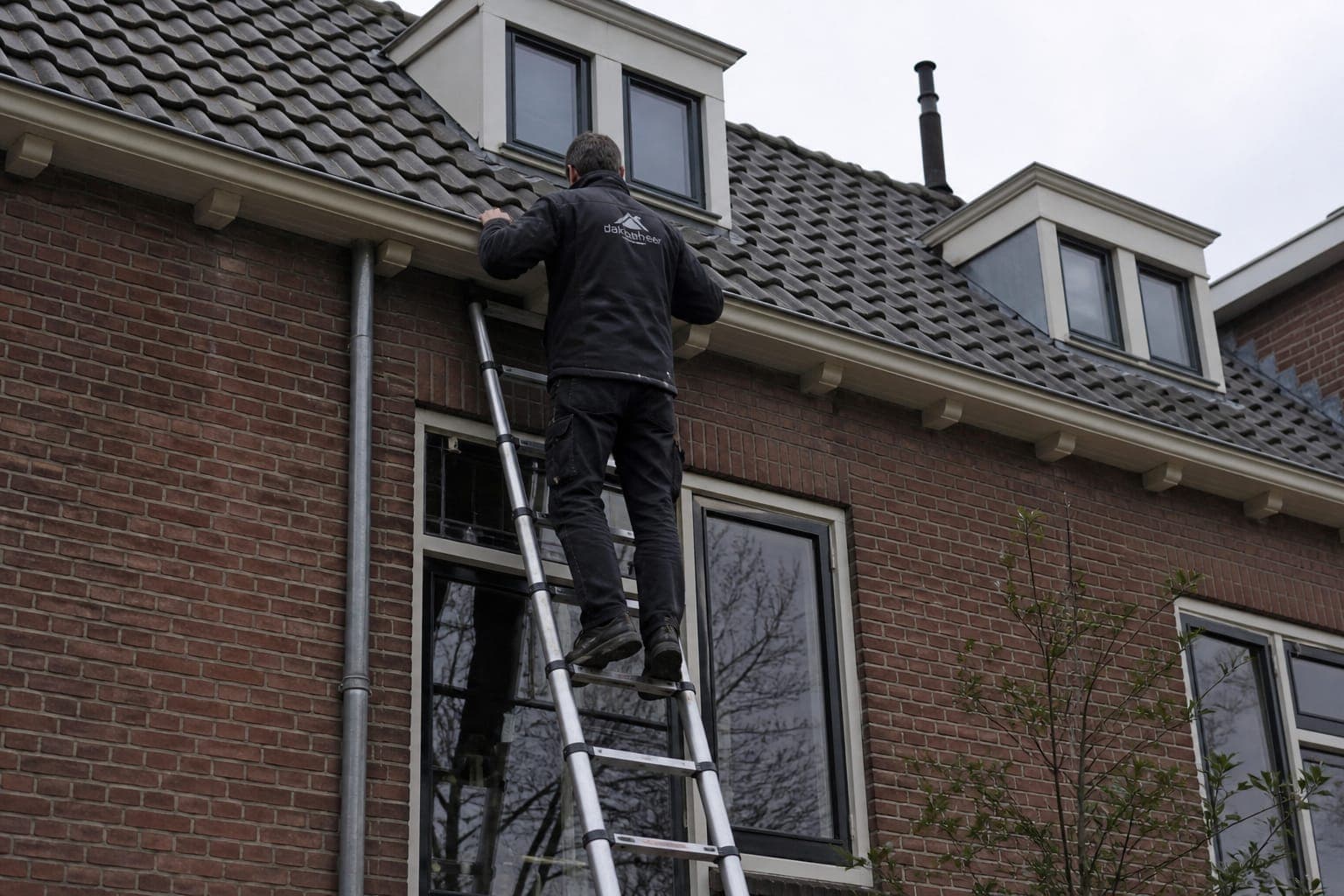 Dakdekker inspecteert het dak en de goot vanaf een ladder